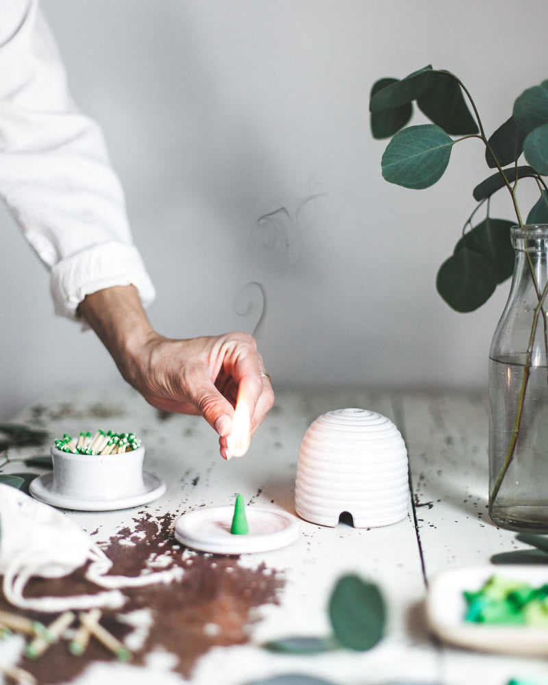 Hand lights Farmhouse Pottery - Artisan Incense Cones: Cedarwood on a white dish, with a beehive cover and eucalyptus, creating a calming, mindful ritual scene.