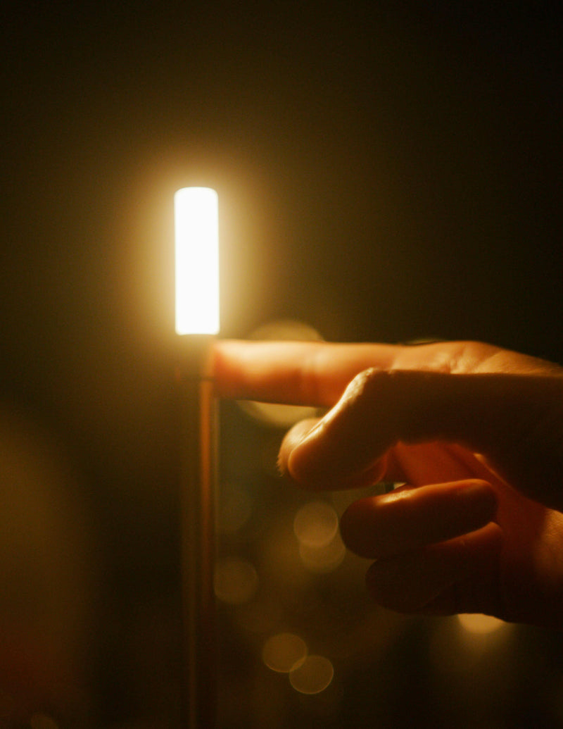 Finger pointing at VANMOKUM | GRAYPANTS Wick Portable Rechargeable Lamp, highlighting its candle-like ambiance and utility, perfect for creating gatherings and shared moments.