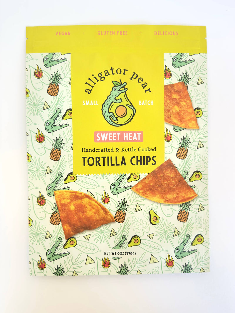 Alligator Pear Foods - Sweet Heat tortilla chips, 6oz package featuring a cartoon alligator, known for sweet pineapple and spicy cayenne flavor. Gluten-free and resealable.
