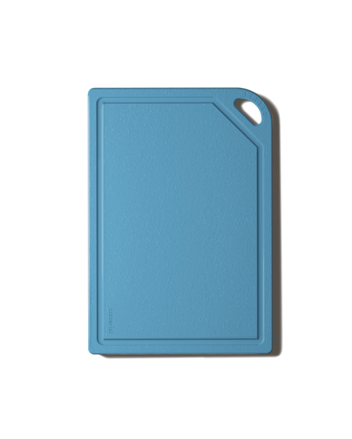 The MK Free Board: Ocean, a sky-blue kitchen cutting board with a textured surface, raised edges, and a corner handle for easy use and storage.