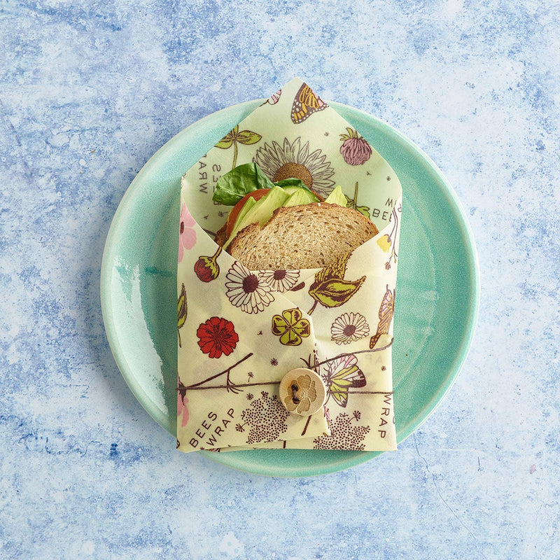Bee's Wrap - Sandwich Wrap - Meadow Magic, Vegan Wax secures a veggie sandwich, showcasing a reusable wrap with a wooden button and twine on a kitchen plate.