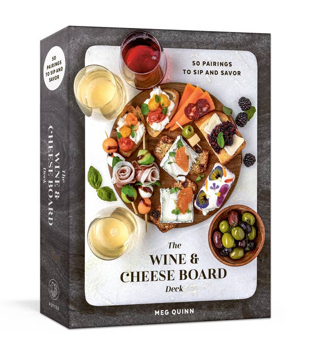 Packaging for The Wine & Cheese Board Deck by Meg Quinn, depicting a wooden board with assorted pairings, three wine glasses, and olives, highlighting 50 pairing ideas.