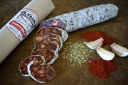 Olympia Provisions - Chorizo Rioja, sliced on a board with its labeled sleeve, garlic cloves, oregano, and paprika, highlighting its signature Spanish flavors.