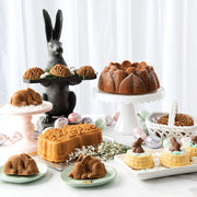 Nordic Ware | Baby Bunny Cake Pan amid cakes and bunny-themed decor, showcasing its detailed design and generous capacity for baking adorable bunny-shaped cakes.