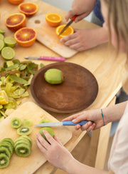 Two people prepare fruit using the Opinel | Essential Birdsbeak Vegetable Knife, showcasing its precision in slicing kiwis and oranges on a kitchen table.