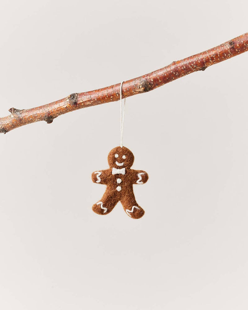 Farmhouse Pottery - Felted Gingerbread Ornament: Gentleman, handcrafted in Nepal, features white icing details, hanging from a tree branch. Made of 100% wool.