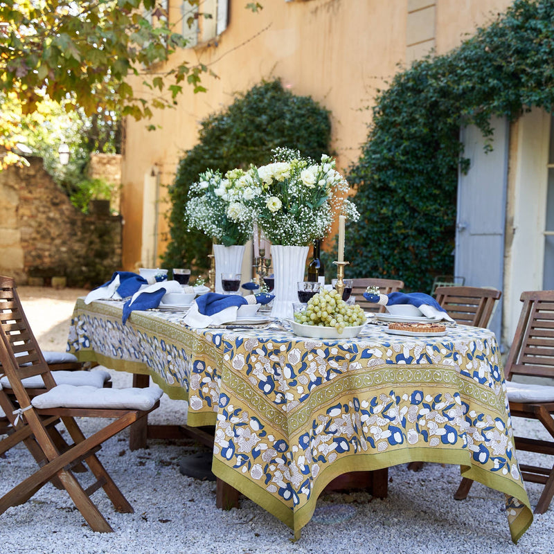 Couleur Nature - Forest Harvest Mustard & Blue tablecloth adorns an al-fresco dining setup, featuring elegant ceramics and lush floral centerpieces in a Mediterranean-inspired courtyard.