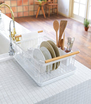 Yamazaki Home | Steel + Wood Dish Rack with Drainer Spout on a bright kitchen counter, holding plates, glasses, and utensils in a stylish, functional design.