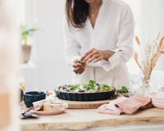 A person adds herbs to a tart in a dark fluted pan on a wooden board, reflecting a culinary moment with the Emile Henry Focaccia + Detroit Pizza Pan, Charcoal.