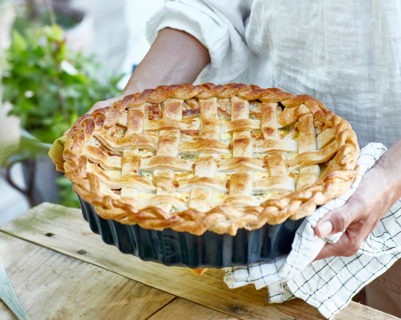 Person holding a freshly baked pie in a round dish, highlighting the craftsmanship of the Emile Henry Modern Classics Loaf Pan, Rouge, 9 x 5.
