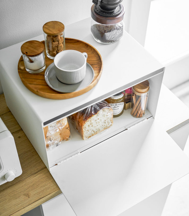 Yamazaki Home | Simple Steel Bread Box, White + Wood, on a countertop, holds bread and jars, topped with a coffee setup, next to a toaster.
