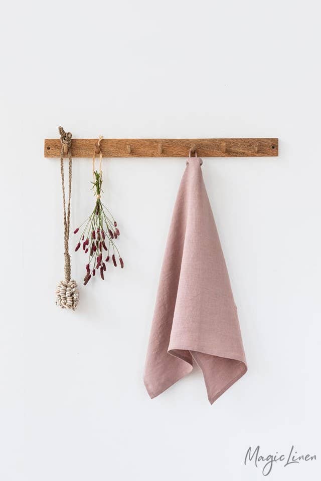 Linen tea towel hanging on a wall, showcasing its texture and loop for easy hanging; a practical kitchen accessory from Athens Cooks.