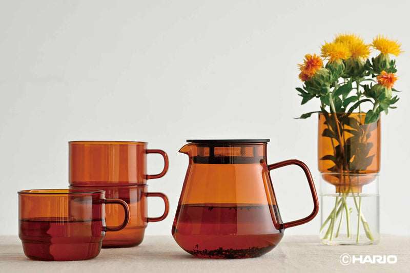 HARIO USA - HARIO Colors Glass Stackable Mug, 300ml: Grey, displayed with an amber teapot and vase, showcasing durable, vibrant heatproof glassware.
