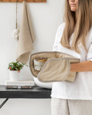 Woman holding a potted plant, showcasing MagicLinen's Forest green gingham double oven mitt, designed for heat protection and part of a zero-waste initiative.