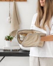 Woman holding MagicLinen - Double oven mitt: Cinnamon gingham, designed for heat protection in cooking, part of a zero-waste program by Athens Cooks.