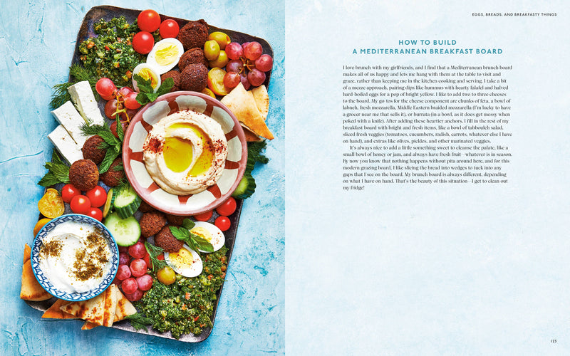 Penguin Random House LLC - The Mediterranean Dish: A cookbook spread showcasing a vibrant Mediterranean mezze breakfast board with dips, veggies, pita, and cheeses, alongside assembly tips.