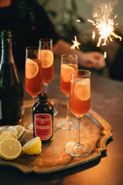 Bittermilk Bottling Co. - No.4 New Orleans Style Old Fashioned Rouge cocktail mixer bottle on a tray with glasses, lemons, and barware.