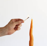 Hand lighting the Artifaqt - Carrot Taper Beeswax Candle: Orange, shaped like a carrot, showcasing its unique design and craftsmanship.