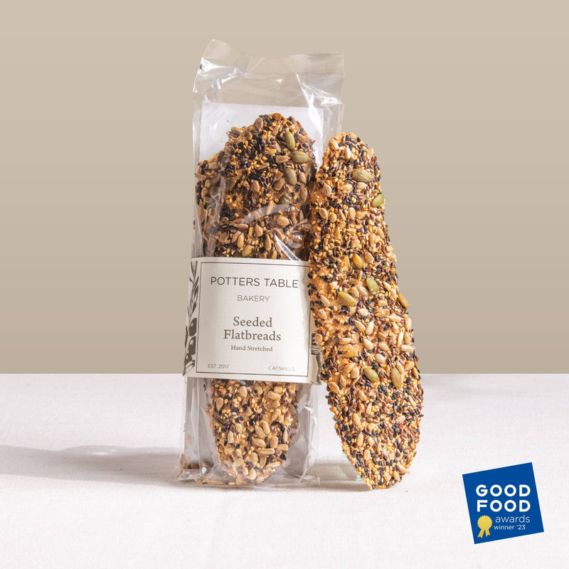 Potters Table - Seeded Olive Oil Flatbreads, artisanal crackers with mixed seeds, clear-packaged, showcasing a Good Food Awards Winner '23 badge. Ideal for cheese boards and elegant gatherings.