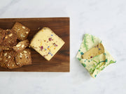 Bee's Wrap - Assorted 3 Pack - Herb Garden, Plant Based Wax shown with cheese on a wooden board, perfect for preserving plant-based foods sustainably.