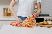 Bee's Wrap - Bread Wrap - Mushroom Magic, Limited Edition: A reusable wrap secures a partially sliced loaf on a kitchen counter, with bread slices on a cutting board nearby.