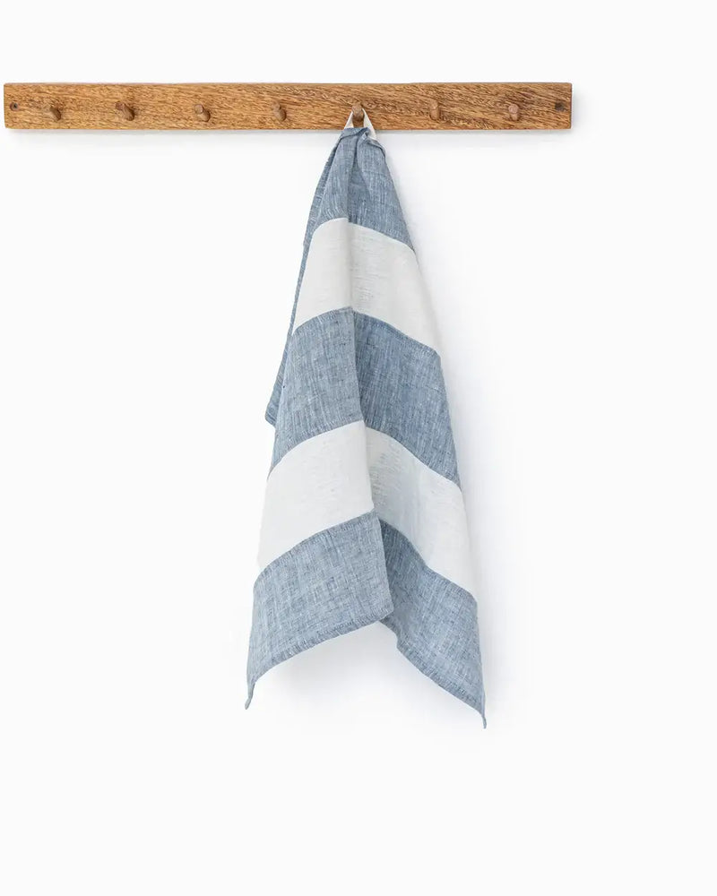 Striped linen tea towel on a hook, showcasing its hanging loop feature. Part of a zero-waste program, it's durable, soft, and absorbent.