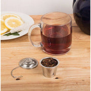 HIC Kitchen Barrel Tea Infuser, Large, with loose leaf tea, next to a clear mug of brewed tea, lemon slices, and a rock-sugar stirrer on a wooden surface.