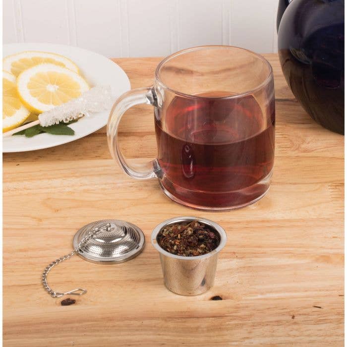 HIC Kitchen Barrel Tea Infuser, Large, with loose leaf tea, next to a clear mug of brewed tea, lemon slices, and a rock-sugar stirrer on a wooden surface.