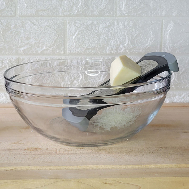 Microplane | Bowl Graters, Fine resting on a glass bowl, grating Parmesan cheese. Ideal for efficient, safe kitchen prep at Athens Cooks.