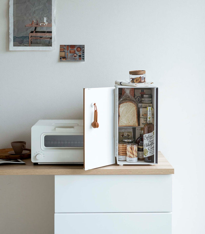 Yamazaki Home | Bread Box, Vertical, Steel + Wood, shown open with bread, drinks, and pantry items inside, next to a toaster-oven on a minimalist kitchen counter.