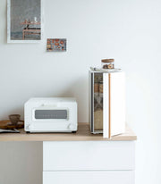 Yamazaki Home Bread Box, Vertical, Steel + Wood, shown open on a minimalist kitchen counter, holding bread and snacks, with a toaster-oven beside it.