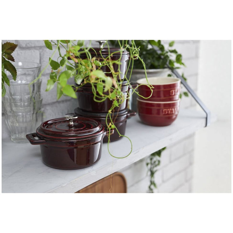 Staub Mini Round Dutch Oven, Grenadine, 0.25 QT, on a kitchen shelf with matching bowls, clear glasses, and a houseplant, embodying Athens Cooks' curated culinary elegance.
