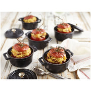 Staub Mini Round Dutch Oven, Black, 0.275 QT., featuring a hollowed tomato with yellow rice, displayed with a fork and napkin on a wooden surface.