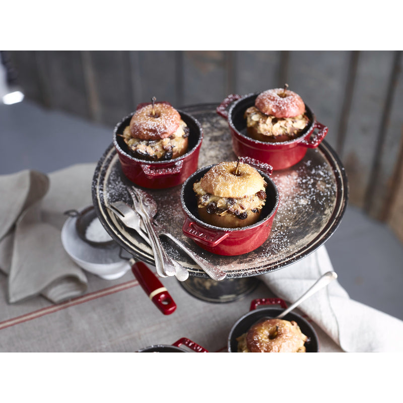 Mini Round Dutch Ovens in Cherry by Staub, 0.275 QT, hold baked apples with raisin-nut crumble, presented on a cake stand.