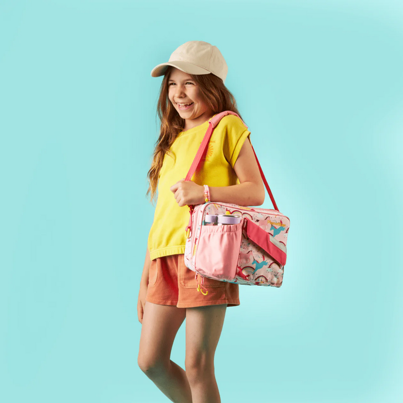 Young girl with a PlanetBox Rover-Launch Carry Bag - Unicorn Magic, featuring unicorns and rainbows, adjustable strap, and a side pocket holding a water bottle.