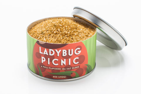 Beautiful Briny Sea's Ladybug Picnic Sea Salt can with lid open, featuring a spoon for serving. Perfect for enhancing culinary creations from Athens Cooks.