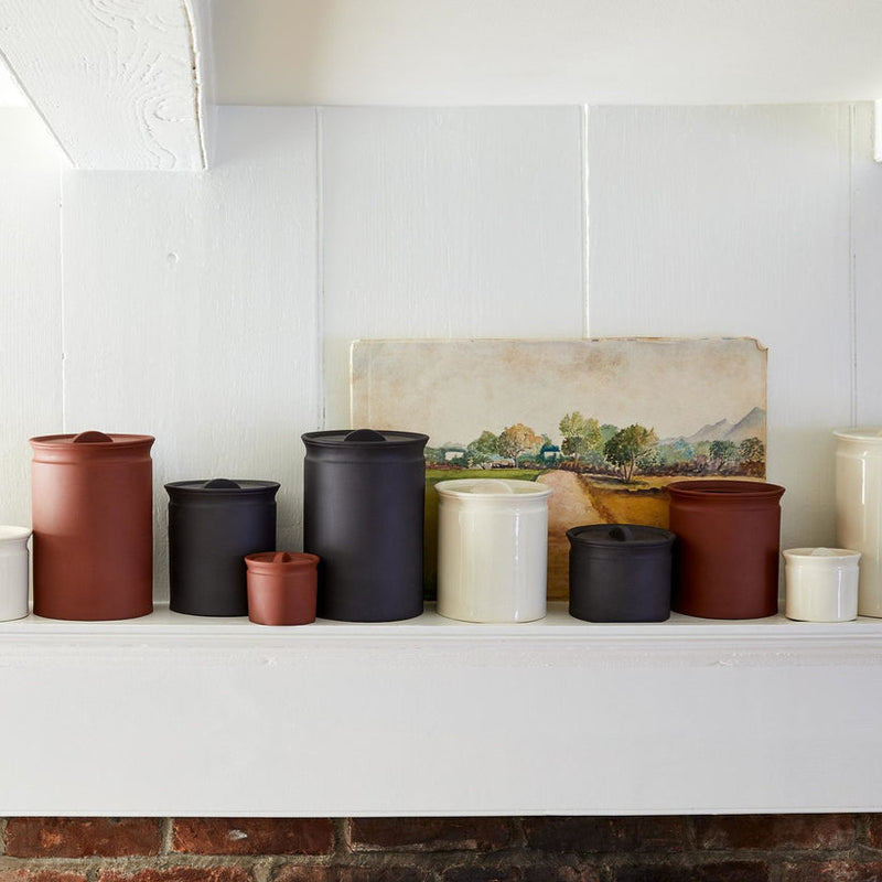 Sir|Madam Terra Cotta Larder Crock No. 10 on a white shelf with other ceramic canisters, exemplifying functional elegance inspired by traditional French preserving jars.