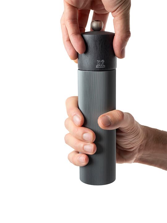 Person holding Peugeot | Line Pepper Mill - Carbon - 9, showcasing its sleek cylindrical design, indicative of high-quality kitchen tools available at Athens Cooks.