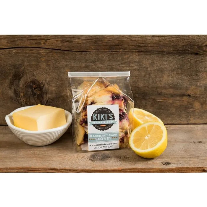 Kiki's Bakeshop Blackberry Lemon Scones in a resealable bag, surrounded by lemon halves and butter, showcased on a wooden surface.