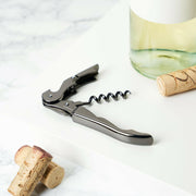 Viski | Warren Signature Waiter's Corkscrew - Gunmetal, featuring a double-hinged arm, 5-turn worm, and integrated foil cutter, displayed on a table with corks.