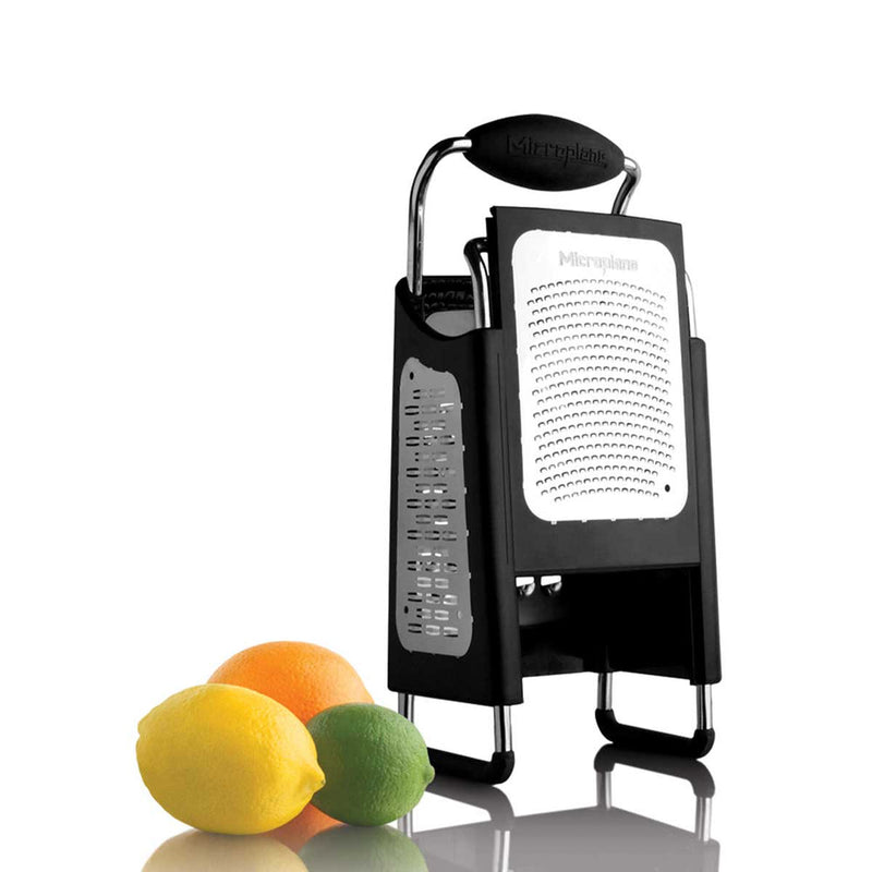 Microplane | 4-Sided Professional Box Grater with interchangeable stainless-steel surfaces beside an orange, lemon, and lime, highlighting its versatility for zesting and grating.