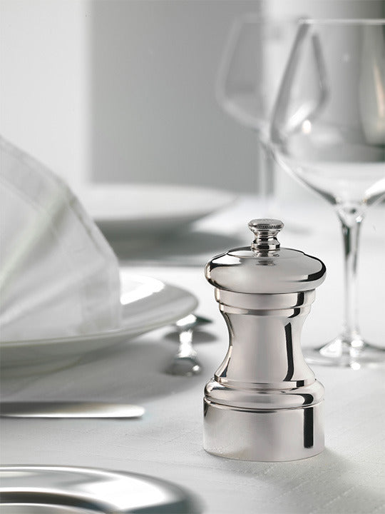 Peugeot Mignonnette Silver Plated Salt Mill, 4 inches, elegantly placed on a refined dining table with white dinnerware, cutlery, and wine glasses, highlighting its sophisticated design.
