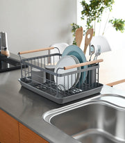 Yamazaki Home | Steel + Wood Dish Rack with Drainer Spout beside sink, holding plates, mugs, utensils; features metal frame, wooden handles, and matching drip tray.