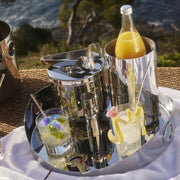 Christofle | Wine Cooler, Stainless Steel, featured on a tray with cocktail glasses and pitcher, set for an elegant outdoor drink service by the water.