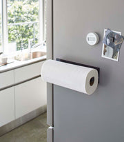 Yamazaki Home Magnetic Steel Paper Towel Holder, White, magnetically attached to a gray fridge in a modern kitchen, holds a fresh paper towel roll.