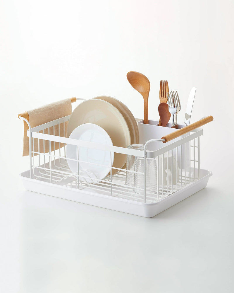 Yamazaki Home | Steel + Wood Dish Rack with Drainer Spout, featuring a sleek design with wooden handles, utensil caddy, and drip tray, holding assorted dishes and utensils.