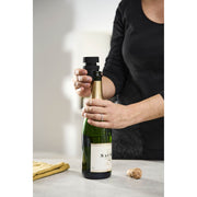A person opens a wine bottle using the Peugeot Preserve Champagne Stopper, showcasing its functionality for preserving opened bottles.