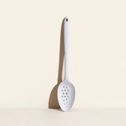 GIR | Ultimate Perforated Spoon - Studio White on table, showcasing perforated design for efficient straining, with a deep bowl and ergonomic handle for versatile kitchen use.