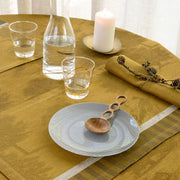 Le Jacquard Francais | Souveraine Napkin, Gold, elegantly tied with twine, complements a warm and minimalist table setting featuring a carafe, glasses, and candle.