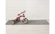 Red tricycle on a rug next to Chilewich Heathered Shag Mat in Fog, showcasing durable, quick-drying texture suitable for various spaces.